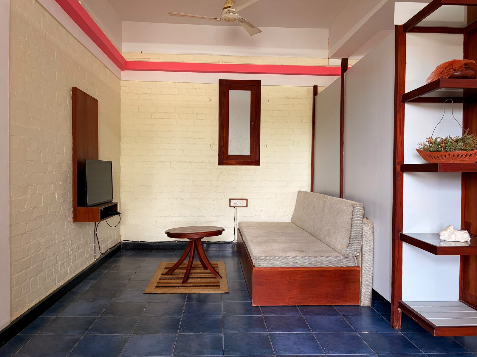 Koodaram sitting area with a daybed, wall-mounted TV, and wooden shelving