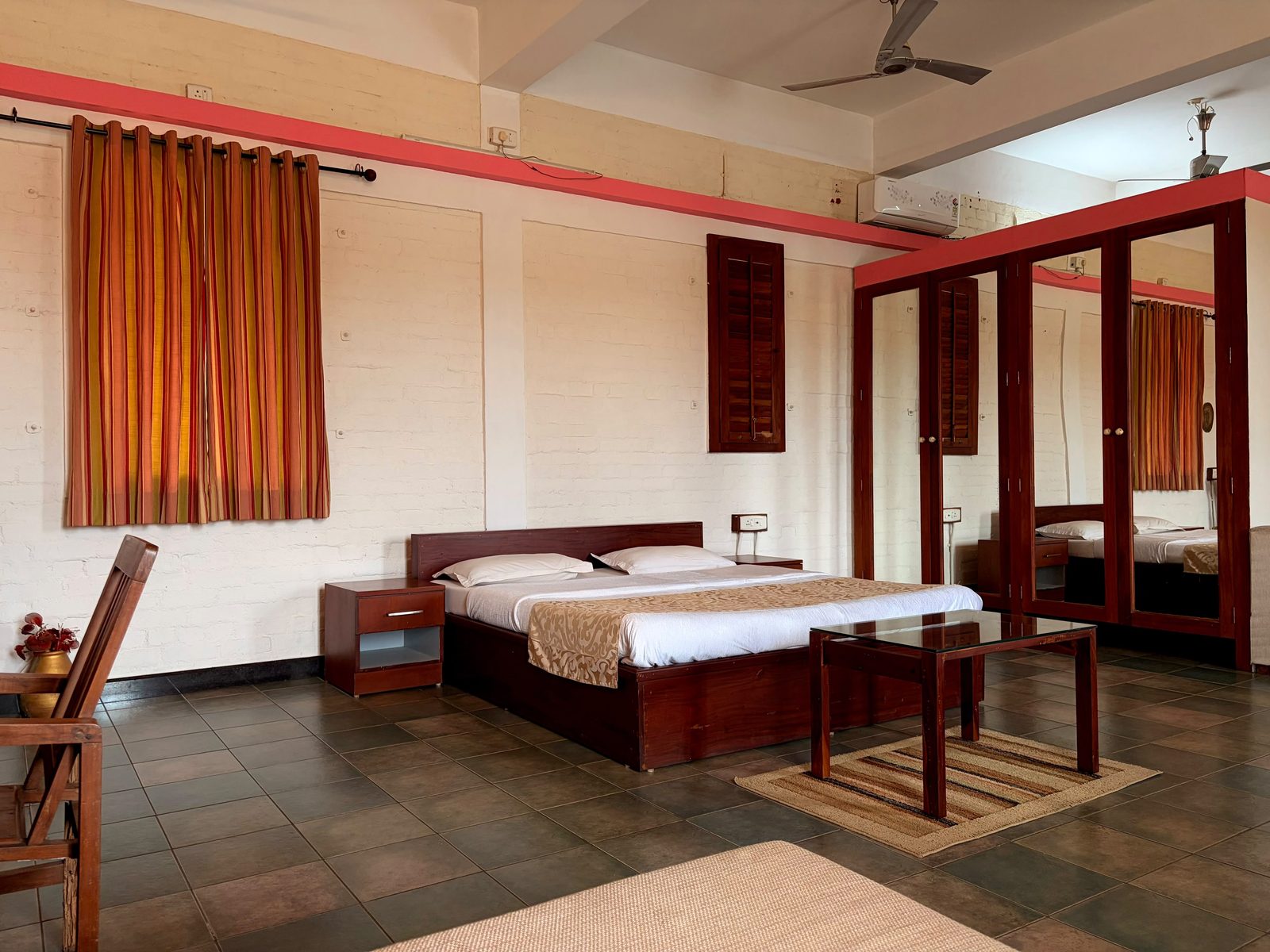 Tharavadu I bedroom with a dark wood bed, mirrored wardrobe, and striped curtains